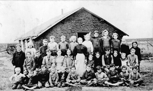Teacher and children in front of sod schoolhouse