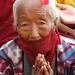 Elder Tibetan woman praying wearing face mask to protect against the dust, and symbolic red blindfold, during Lam dre, Tharlam Monastery, Boudha, Kathmandu, Nepal