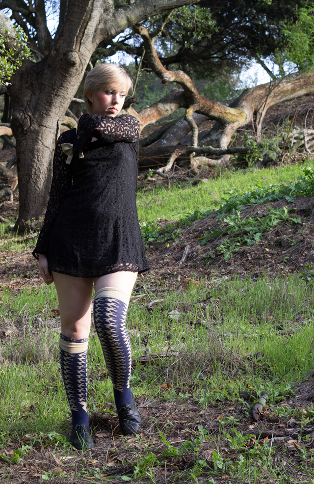 black lace mini dress with bell sleeves, gold bow brooch, knee socks with bird pattern
