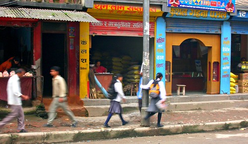 Typical street scene in Kathmandu, men walking, school girls in gray uniforms with backpacks on the sidewalks, brightly painted storefronts with Nepalese writing, Nepal by Wonderlane