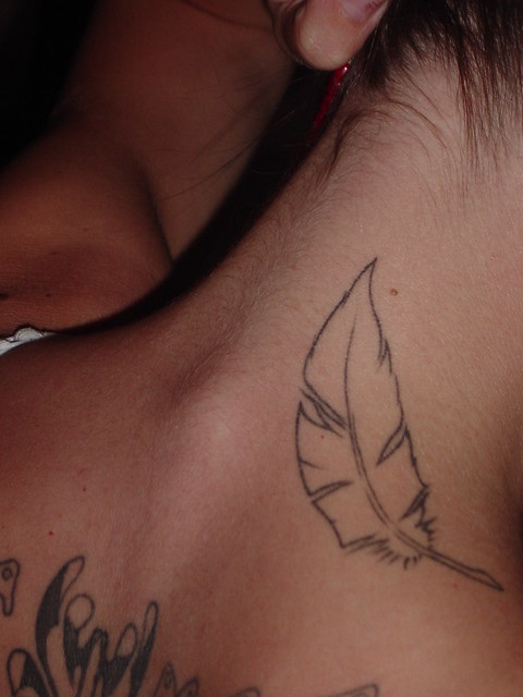 A fine line feather at the base of the neck creates an elegant tattoo 