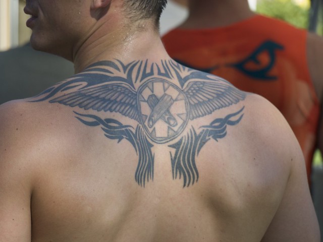 Back tattoo consisting of crossed index fingers wings and tribal detail