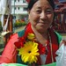 Tibetan Woman with flower and katag offerings, wearing a dZi stone ring, memorial wrist bracelet to Tibetan prisoners, and mala, Tharlam Monastery Courtyard, Boudha, Kathmandu, Nepal