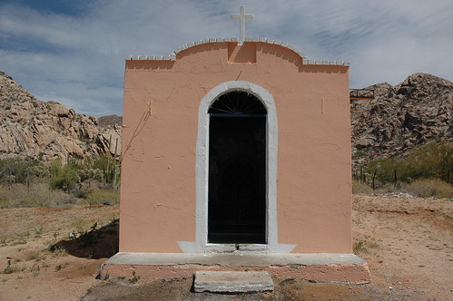 Small pink roadside shrine or chapel, white cross, similarly colored hills and pink rock, Sonora Desert, northern Mexico, along the border, Highway 2 by Wonderlane