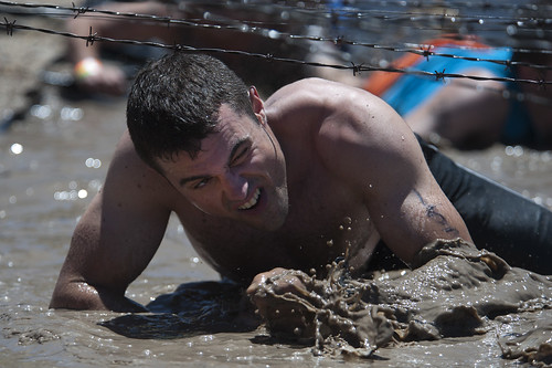 Sailor crawls through the mud on his way through the third obstacle of the Tough Mudder competition by Official U.S. Navy Imagery