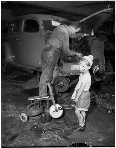 Young boy with dinky in car workshop while his father (?) services a car, Bondi, 6 October 1955 / Ern McQuillan by State Library of New South Wales collection