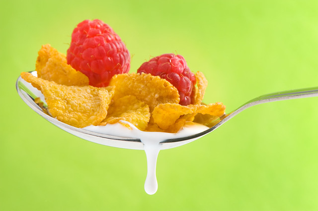 spoon with corn flakes and raspberry on green background