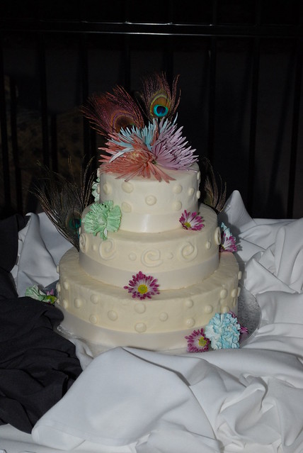 3 tier wedding cake decorated with fresh flowers and peacock feathers