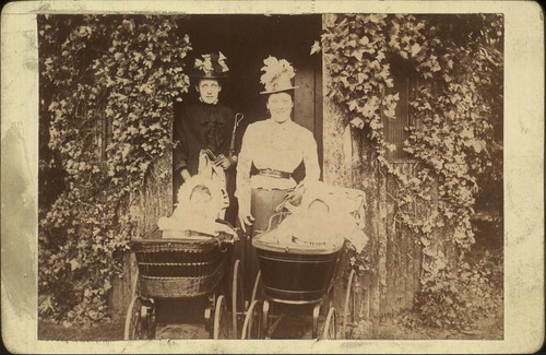 Outdoor posed photograph of two women setting out on a walk with their babies in prams, 1890-1900.