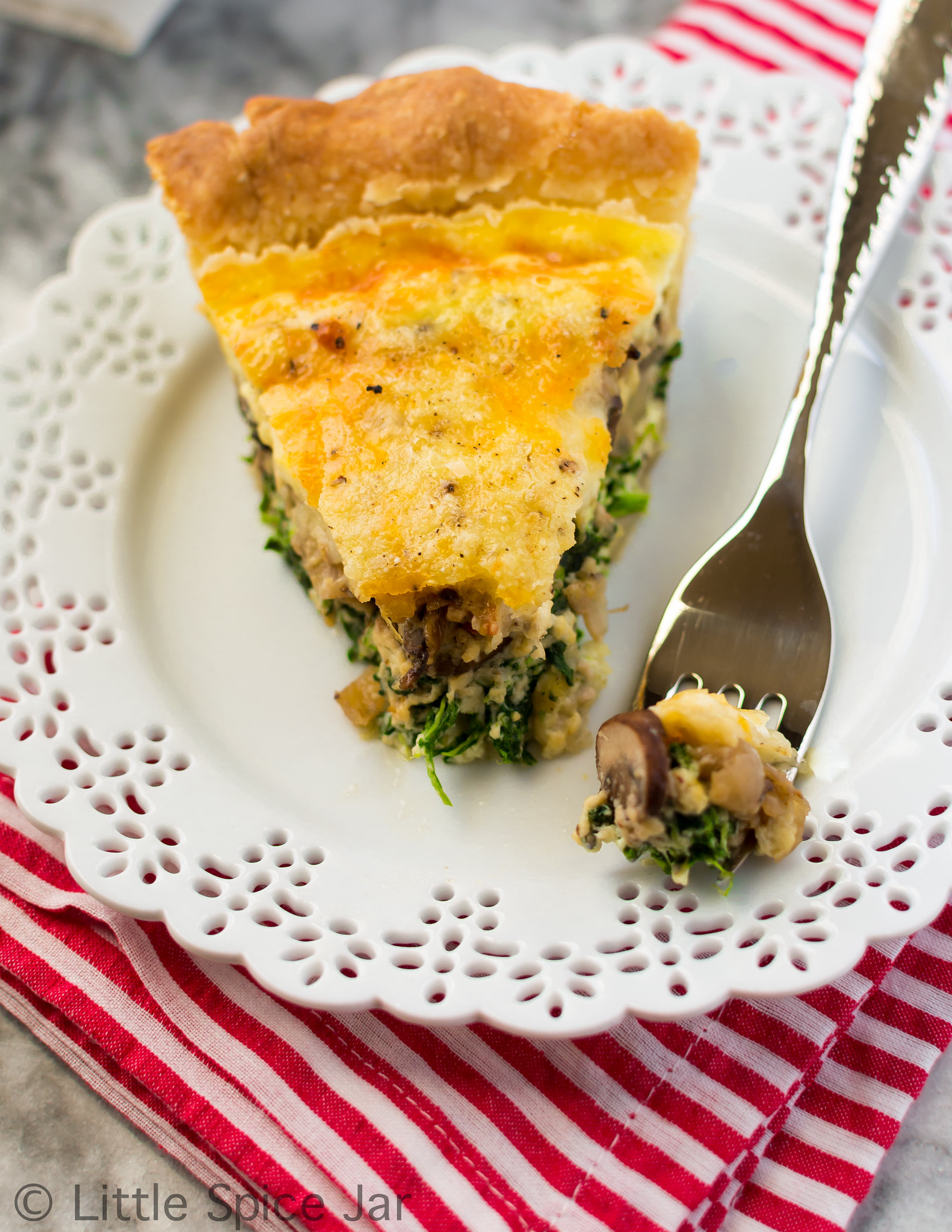spinach mushroom quiche slice on white plate with fork on striped napkin