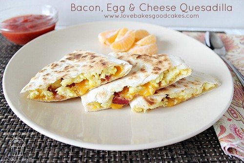Bacon, Egg & Cheese Quesadilla stacked on plate with orange slices and salsa.