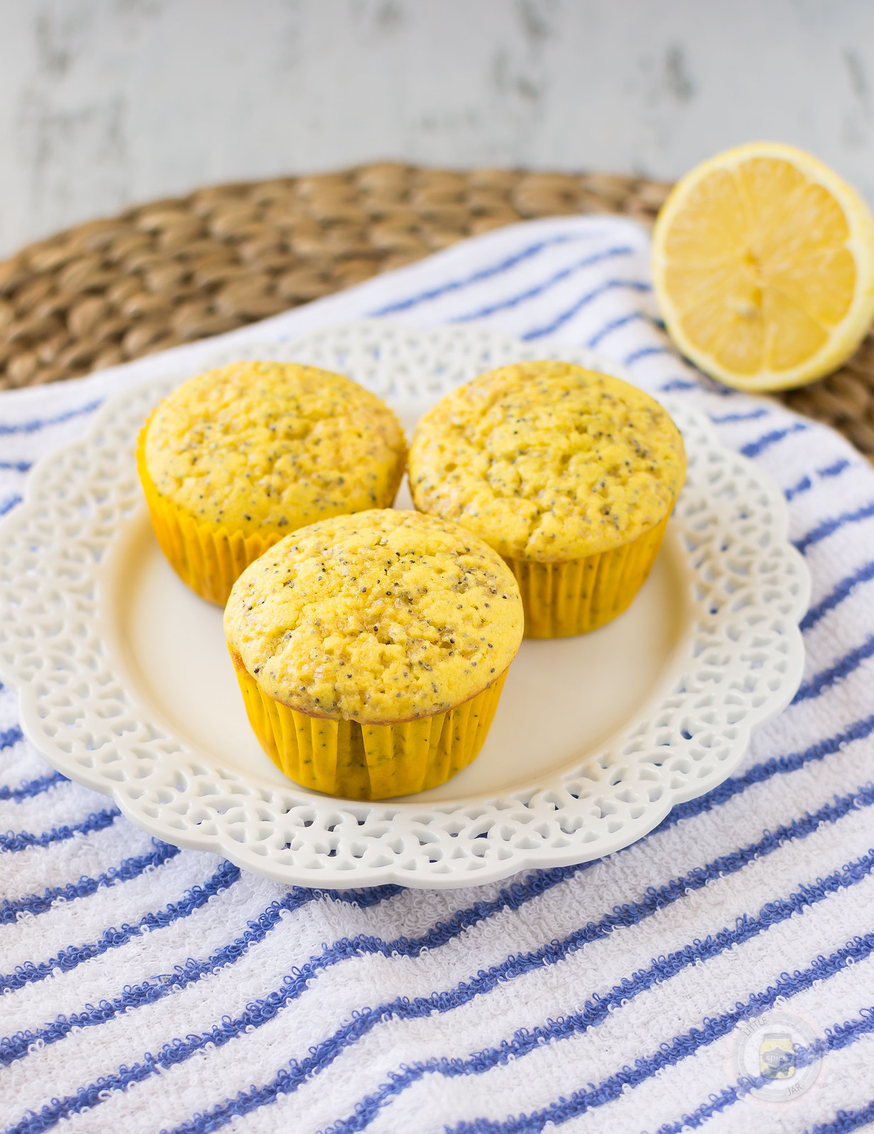 three lemon poppy seed muffins on doily plate on striped hand towel