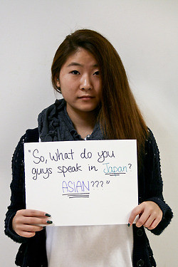 A woman stands with a sign "So what do you guys speak in Japan, Asian?"