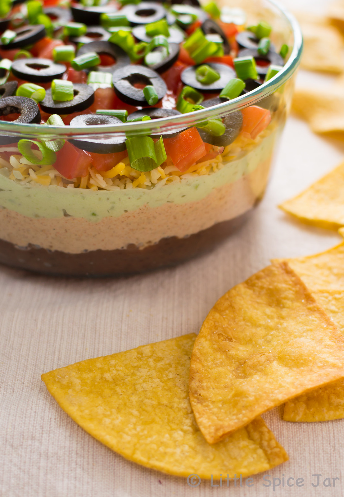 showing layers of skinny seven layer tortilla dip on white surface with homemade tortilla chips