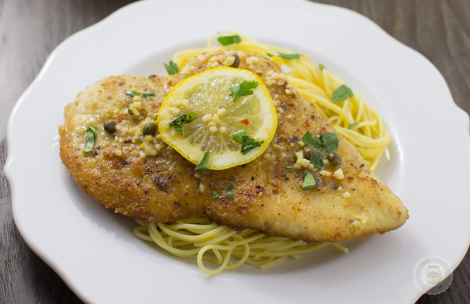 close up of chicken piccata on plate topped with lemon slice and parsley