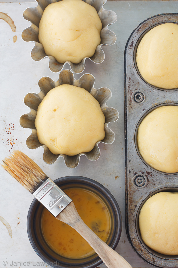 Brushing brioche buns with an egg wash using a pastry brush before baking.