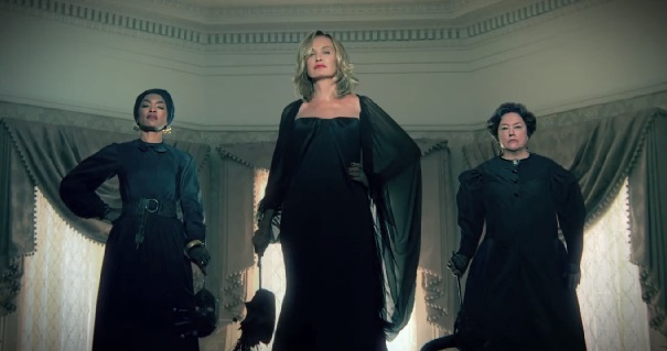 Jessica Lange stands in the middle of three witches dressed in black