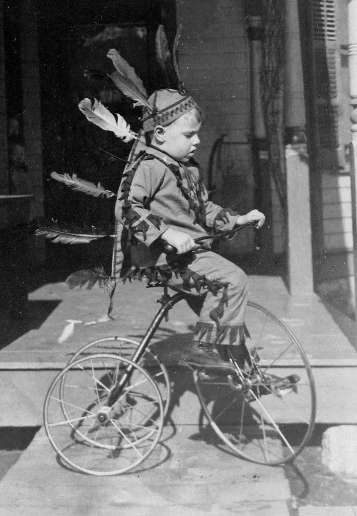 Playing in a head dress on a tricycle.