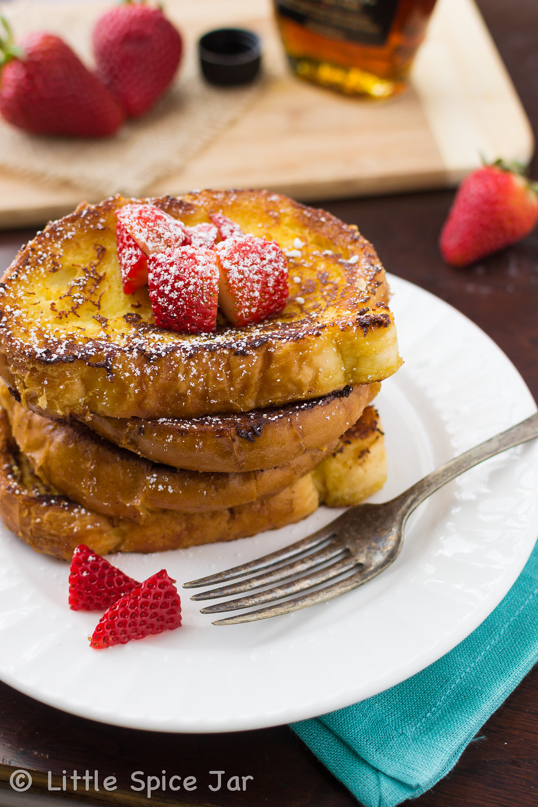 stack of French toast on white plate with fork and strawberries
