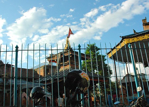 Street view: motorcycle helmets and shrine buildings, metal fence, blue sky with a few puffy clouds, Kathmandu, Nepal by Wonderlane