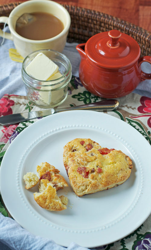 Two strawberry scones on a plate next to a jar of butter and tea