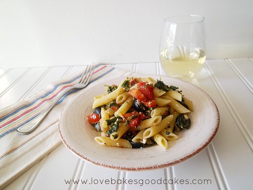 Greek Pasta in bowl with fork and a glass of wine front view.