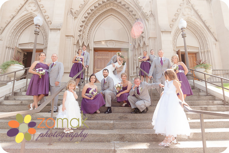 The groom dips his bride with wedding party on the stairs of st helena cathedral on their wedidng day