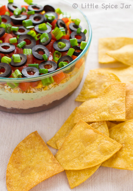showing layers of seven layer dip with scattered tortilla chips on the side