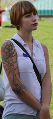 Young girl, a high school student,  with large tatoo of tree on arm, standing listening.