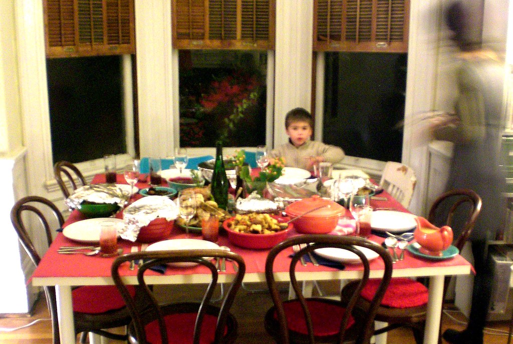 A little boy sitting at the head of the table filled with a Thanksgiving feast