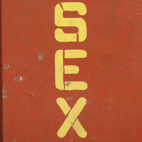 A red wall w/ the words "Sex" spray-painted on it in yellow