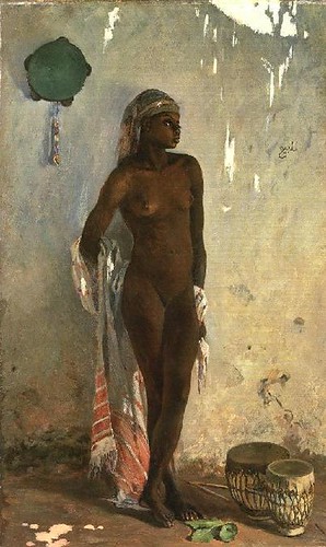 Black woman, nude, in headwrap, standing in front of wall.