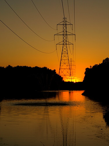 trees sunset sky orange fountain lines canal pond power suburbia pylon wires electricity
