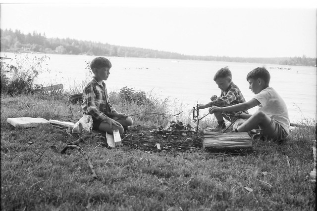 Boys around a campfire by the water.