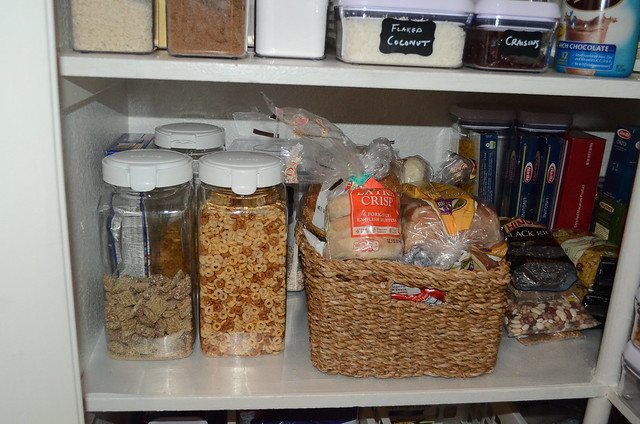 Plastic containers with cereal and a basket with breads in a pantry.