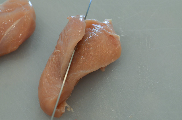 A knife slices through the center of a boneless skinless chicken breast.