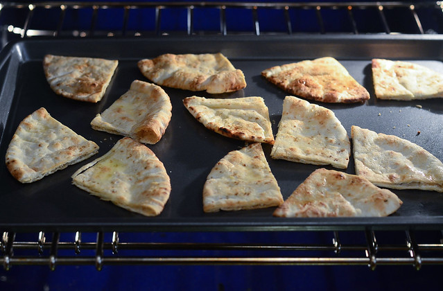 The slices of pita are arranged on a baking sheet and placed in an oven.