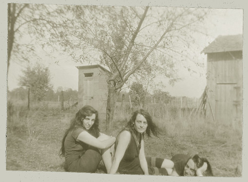 Three girls posing in front of the outhouse