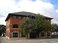 A detached three-storey building built of red brick, with trees in front and car parking to the side and the back.