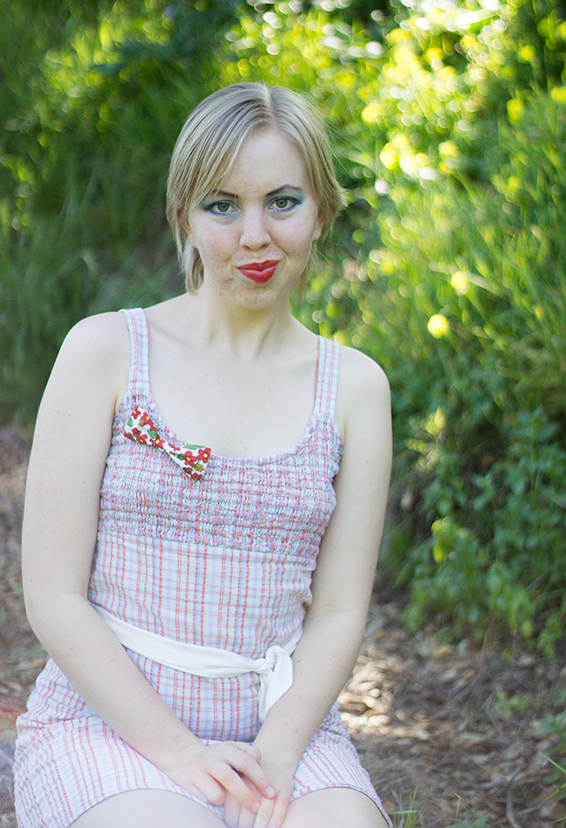 bright red lipstick, red floral bow brooch, pastel plaid dress, white sash