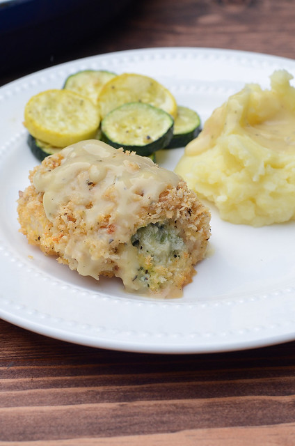 A serving of Broccoli Cheese Stuffed Chicken on a white plate with potatoes and zucchini.