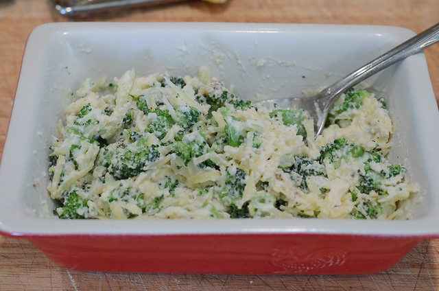 Broccoli is combined with ricotta and Swiss cheese in a red dish.