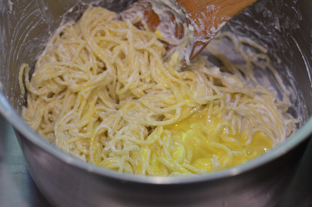 The spaghetti mixture is stirred with a wooden spoon.