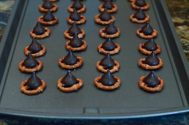 Round pretzels topped with Hershey's Kisses on a baking sheet.