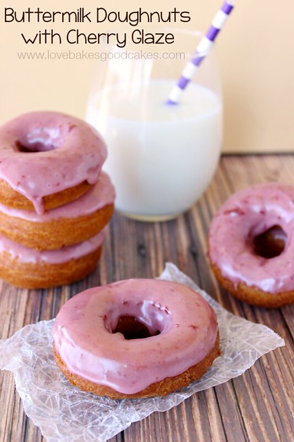 Buttermilk Doughnuts with Cherry Glaze stacked up and laying on a piece of wax paper with a glass of milk and a straw.