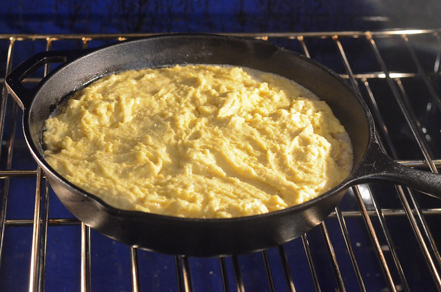 A cast iron skillet with cornbread batter bakes in the oven.
