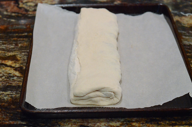 Bread dough stuffed with Italian sausage on a parchment paper lined baking sheet.