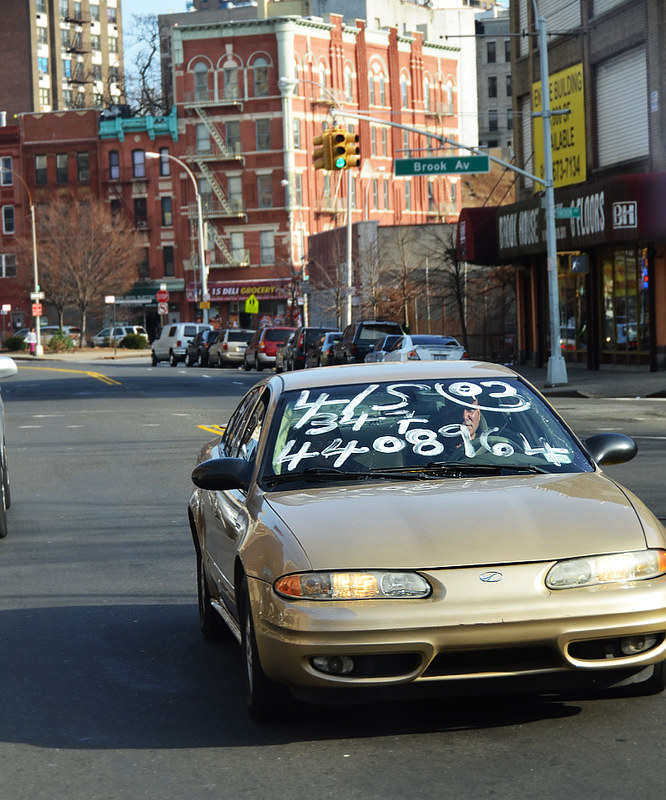 Coche en venta con el cristal delantero pintado paseando por las calles del Bronx