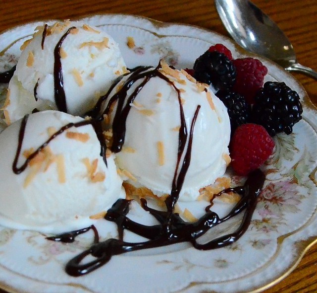 Coconut Ice Cream on a decorative plate with chocolate sauce drizzled on top and a side of raspberries and black berries.