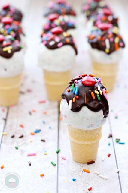 Ice Cream Cone Cake Pops with chocolate syrup and rainbow sprinkles standing up on counter.